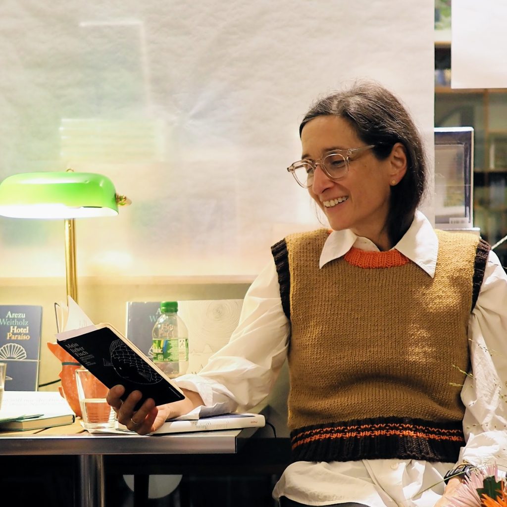 Arezu Weitholz sitzt an einem Tisch vor einer Leselampe und liest aus ihren Fischgedichten